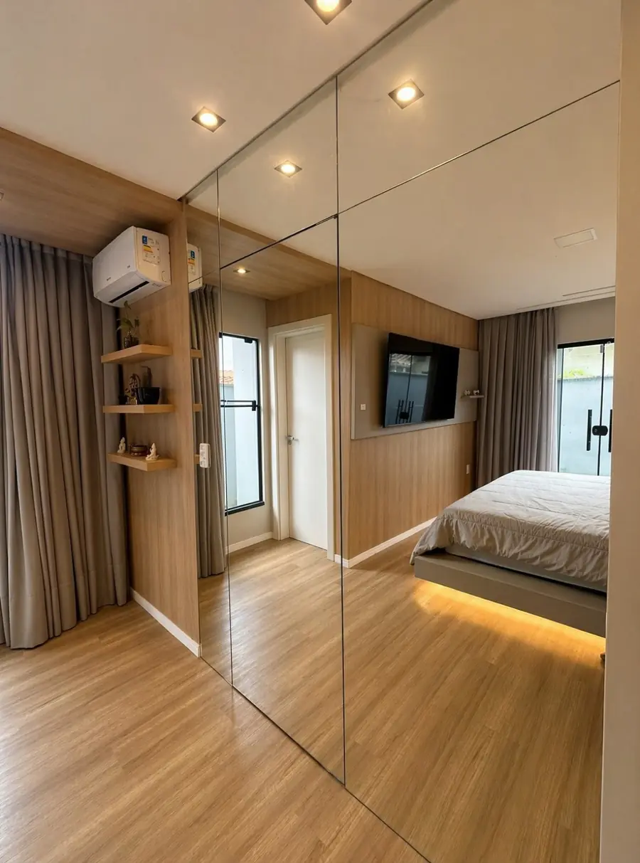 Quarto com porta de espelho de piso a teto refletindo a cama, com fita de LED acesa sob o box.