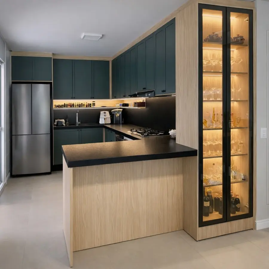 Cozinha em L com armários verde-petróleo, bancada preta e vitrine iluminada para taças e vinhos.