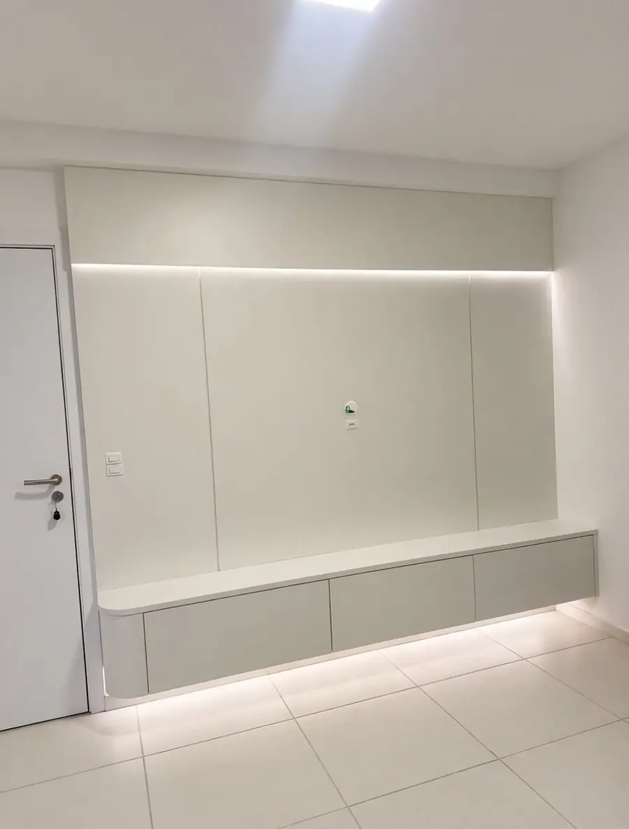 Painel branco liso com iluminação embutida em fita de LED e banco suspenso com gavetas, sem TV instalada.