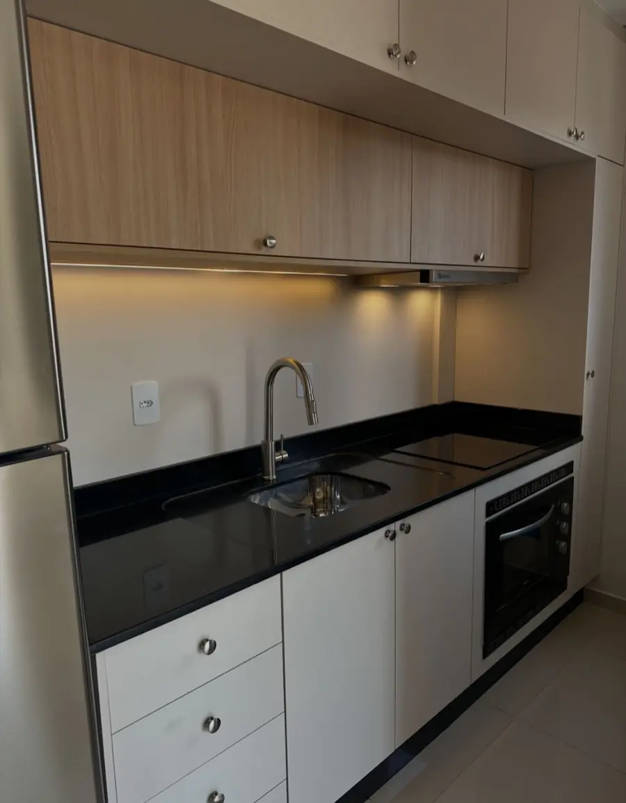 Cozinha em L com armários brancos, tampo de granito preto e geladeira inox ao lado.