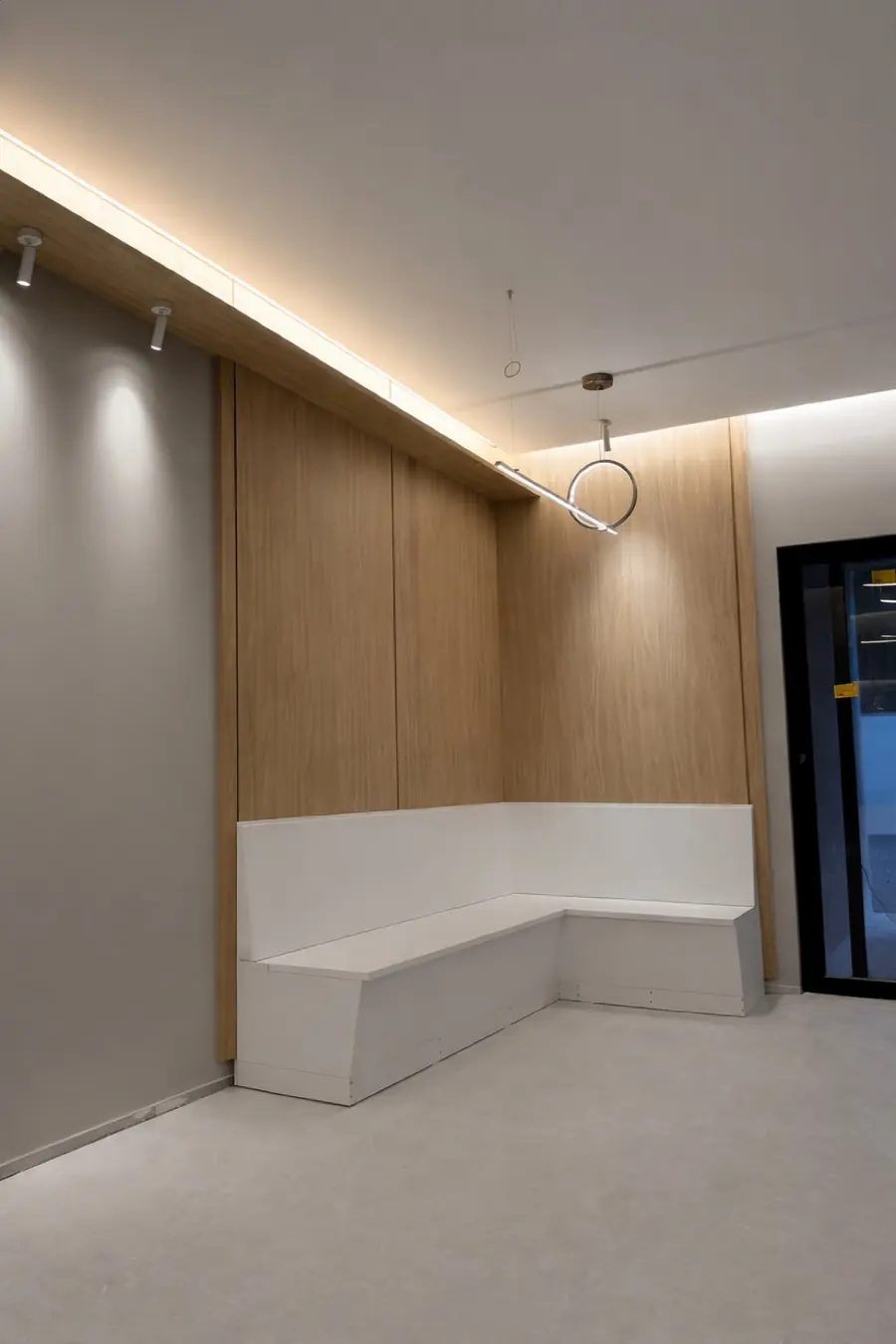 Banco branco em formato L sob painel de madeira com iluminação embutida e luminária circular pendente.