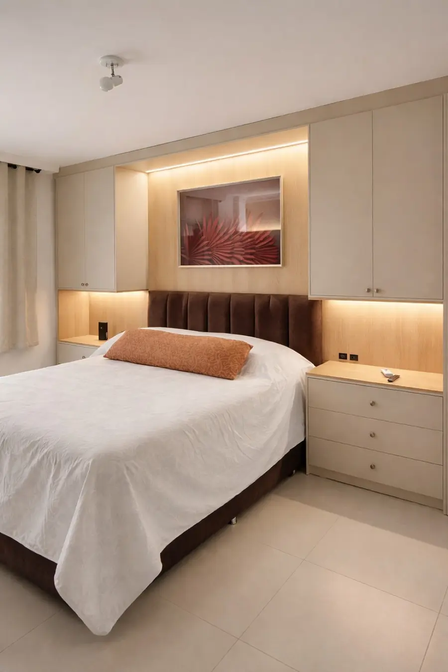 Quarto com cabeceira acanalada marrom, guarda-roupas embutidos bege e luz indireta atrás do quadro.