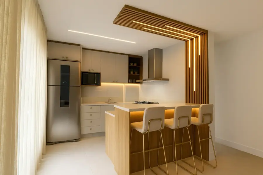 Cozinha compacta com portal de ripas de madeira iluminado e banquetas de metal dourado.