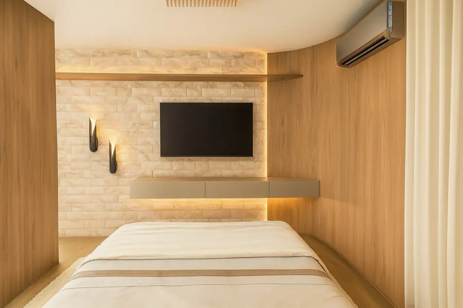 Quarto com parede em tijolinho claro, nicho de TV embutido e arandelas pretas na lateral.